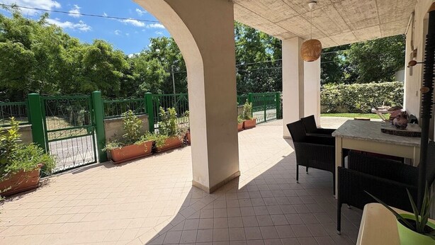 Een buitenterras met een overdekte zithoek, een tafel en plantenpotten.