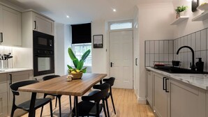 A modern kitchen with a wooden dining table, black chairs, a black oven, and a black sink.