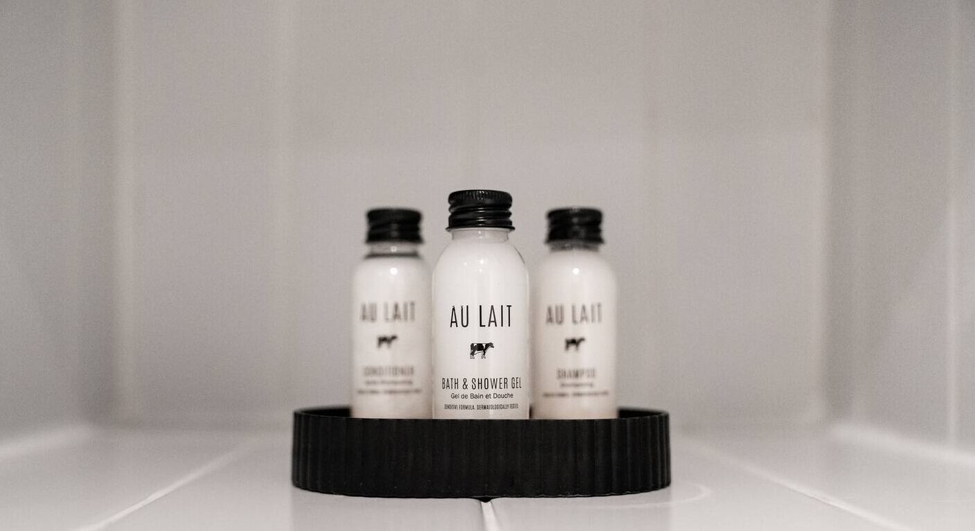 Tres ampolles de gel de bany i dutxa i xampú 'Au Lait' sobre un safata negra a un bany.