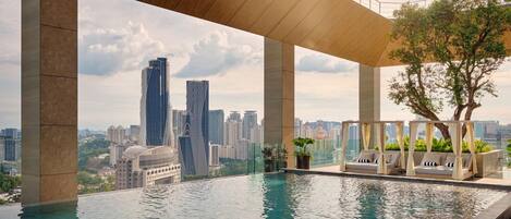 Una piscina infinita con vistas a la ciudad, una pérgola de madera y sillones de descanso.