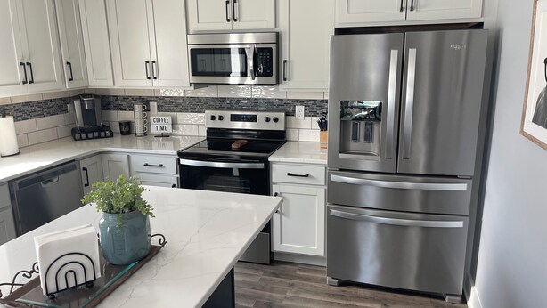 A modern kitchen with white cabinets, stainless steel appliances, a coffee maker, and a potted plant on the counter. - Charming 3-bedroom, 2-12/ bath house with AC, WiFi in peaceful Fortville (Fortville)