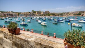 A marina with numerous boats docked, a stone wall, and potted plants along the walkway. - Charming 1-bedroom house with AC, WiFi in beautiful Birzebbugia (Birzebbugia)