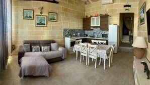 A cozy living room with a sofa and a dining table, a kitchen with a stove and cabinets, and a small statue on a table. - Charming 1-bedroom house with AC, WiFi in beautiful Birzebbugia (Birzebbugia)