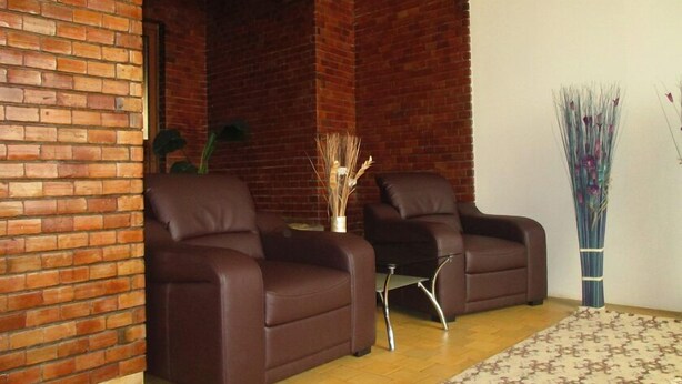 Ein Zimmer mit zwei braunen Ledersofas, einem kleinen Tisch, einer Vase mit Trockenpflanzen und einem gemusterten Teppich auf Holzboden.