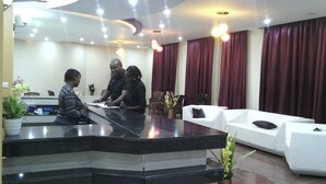 A reception area with a black marble counter, white sofas, and red curtains. - Miale Hotel  (Nakuru)