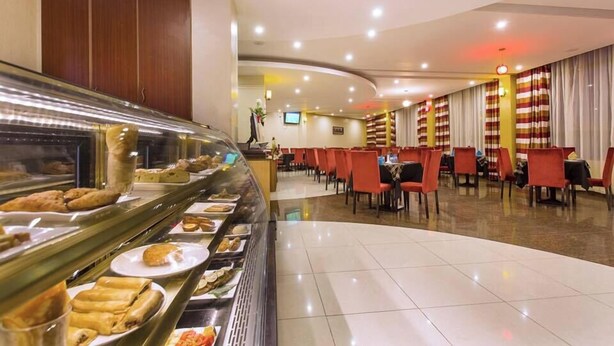 A buffet area with various food items, a seating area with tables and chairs, and a counter with a display case. - Miale Hotel  (Nakuru)