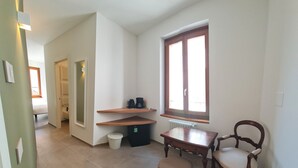 A small, well-lit room with a wooden table, a chair, a bench, a radiator, and a window with blinds.