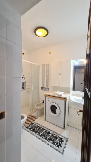 Un baño pequeño con lavadora, inodoro y zona de ducha.
