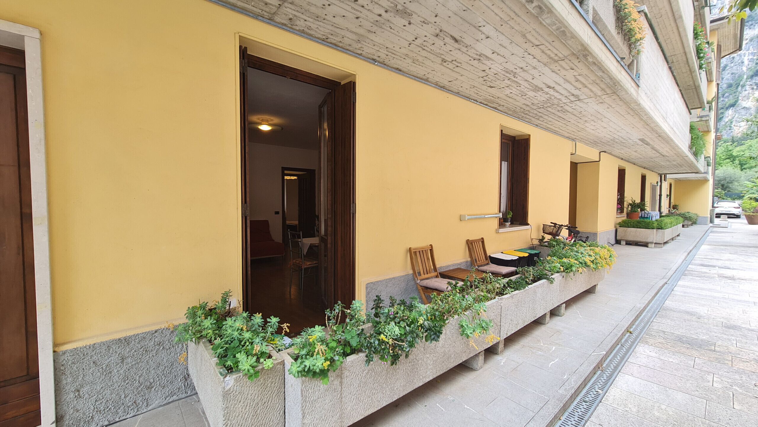 A hotel corridor with yellow walls, wooden doors, and a covered outdoor seating area with chairs and tables.
