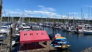 Un port de plaisance où sont amarrés de nombreux bateaux, une tente rouge portant l’inscription « PRYC », et un panneau indiquant « Port du club de yacht de l’île du Prince-Édouard ».