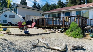 Un véhicule récréatif est stationné dans une cour arrière, à côté d’une terrasse, et est entouré de gravier et de verdure.