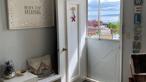 Une pièce avec une porte blanche, un banc, un mur orné d’une inscription « NE CESSEZ JAMAIS DE RÊVER » et une vue sur l’extérieur.