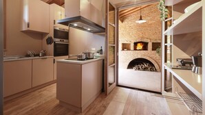 A modern kitchen with a central island, built-in oven, and a brick fireplace. - Agriresort Bacaringhe 13, Emma Villas (Terricciola)