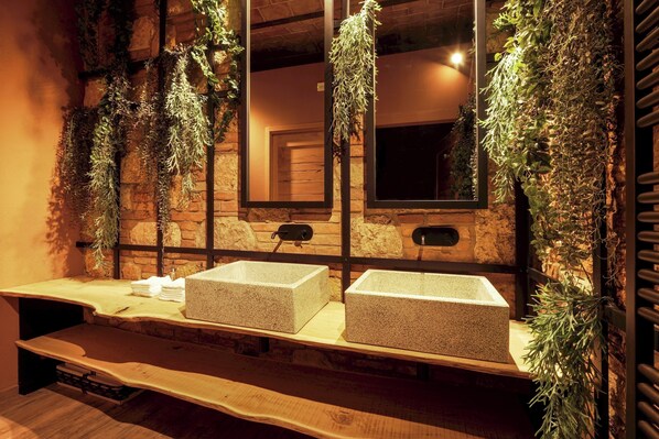 A bathroom with two rectangular stone sinks, a wooden bench, and a mirror with a stone frame.