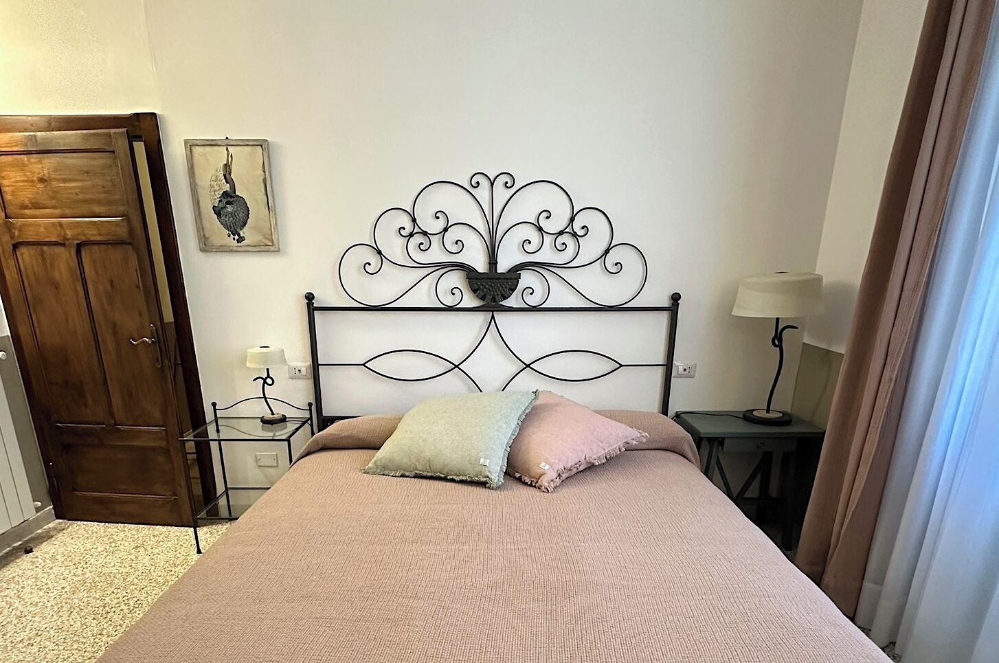 A bedroom with a bed, a wooden wardrobe, a bedside table with a lamp, and a wall-mounted picture.
