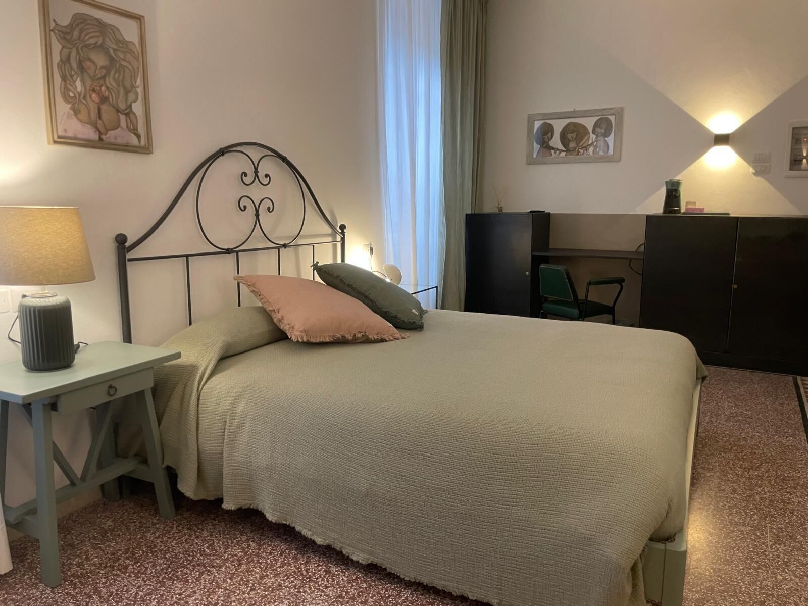 A bedroom with a bed, bedside table, lamp, and a desk with a chair.