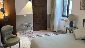 Un dormitorio con cama, una silla, un radiador, una lámpara y una puerta.
