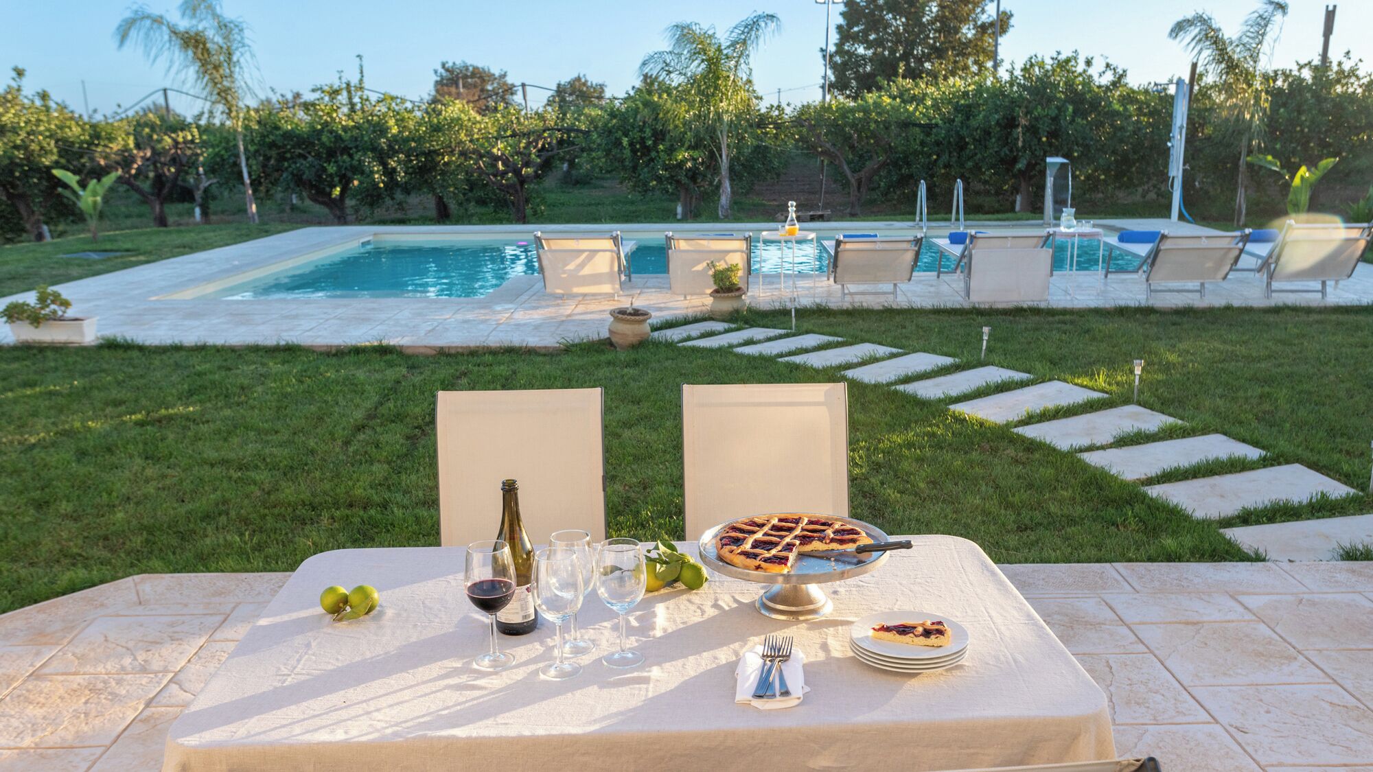 Un espace de restauration en plein air avec une table dressée pour deux personnes, agrémentée d’une bouteille de vin, de verres, d’une assiette de nourriture et d’un dessert.