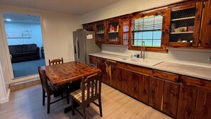 Una cocina con alacenas de madera, un refrigerador de acero inoxidable, un lavamanos y una mesa de comedor con sillas.
