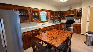 Una cocina con armarios de madera, un refrigerador de acero inoxidable, una mesa de comedor de madera y un microondas.