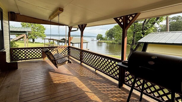 Una terraza techada con una mecedora, una parrilla y vistas a un lago.