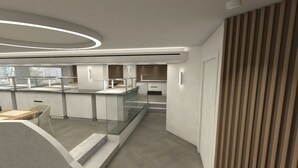Una cocina moderna con una isla central, un comedor con mesa y sillas, y una escalera que conduce a un nivel superior.