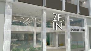 Un hotel moderno con fachada de vidrio, una escalera visible y el nombre 'ZEIN BOUTIQUE HOTEL'.