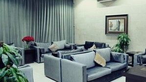 A modern living room with grey sofas, a large window with grey curtains, a framed artwork on the wall, and a potted plant. - In Taiba Apartment (Madinah)