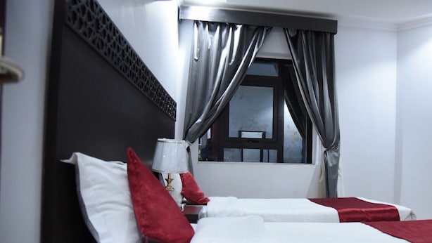 A hotel room with two beds, a window with curtains, a wall-mounted air conditioner, and a decorative wall panel. - In Taiba Apartment (Madinah)