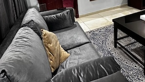 A modern living room with a grey sofa, a coffee table, a TV, and a mirror. - In Taiba Apartment (Madinah)