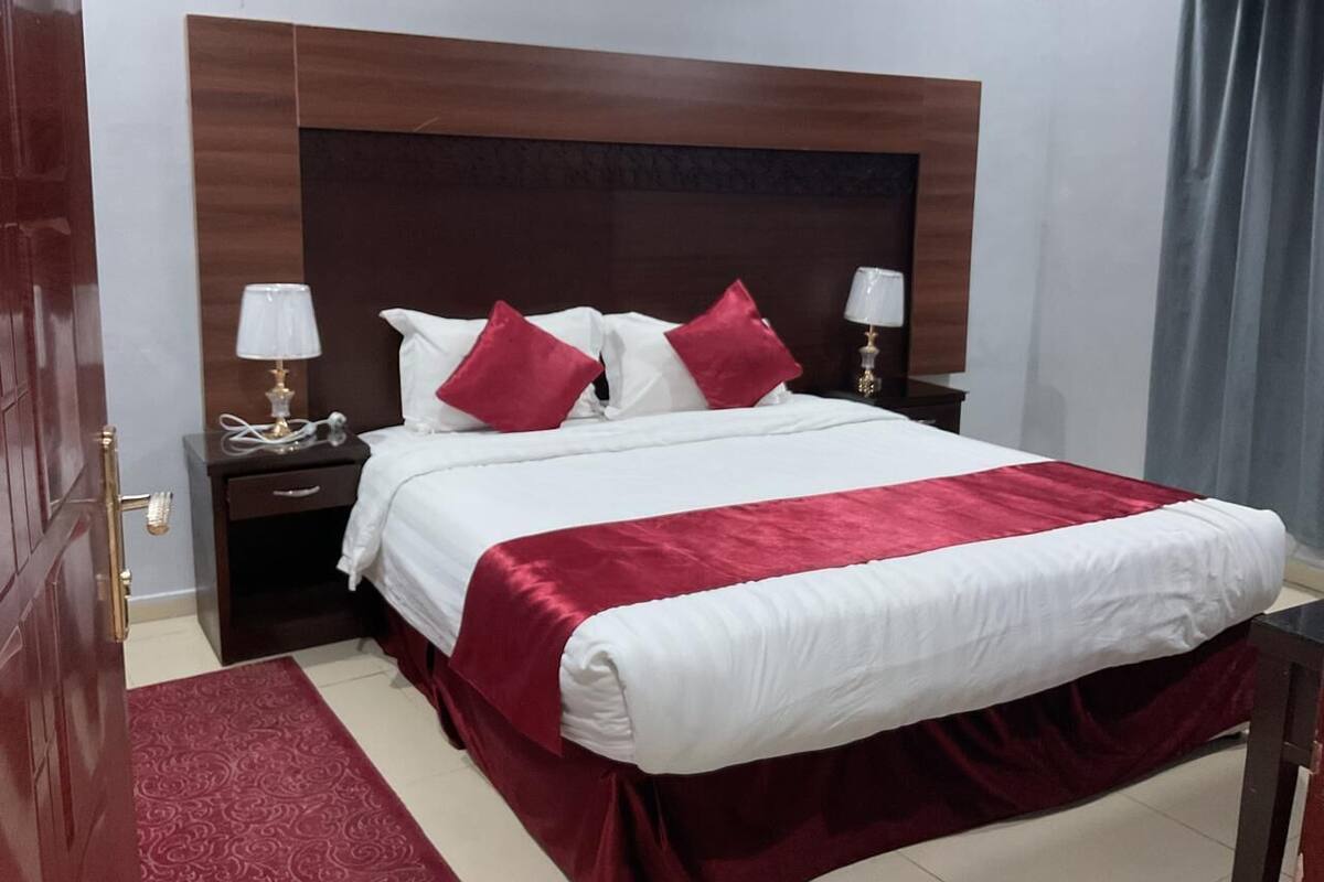 A neatly made bed with white and red bedding, two bedside tables with lamps, and a wooden headboard.