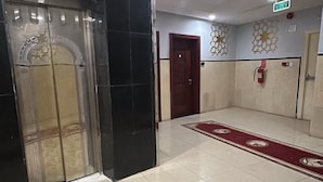 A spacious lobby with a marble floor, a red carpet, and a fire extinguisher on the wall. - In Taiba Apartment (Madinah)