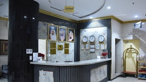 A reception area with a marble counter, framed portraits, clocks, and a reception sign. - In Taiba Apartment (Madinah)
