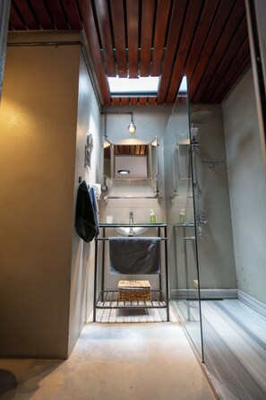 Een compacte badkamer met dakraam, een douchecabine van glas en een klein bankje.