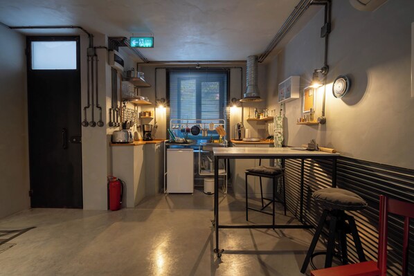 A compact kitchen with a central island, a small refrigerator, and a window with blinds. - Macaron Loft (Ayvalik)