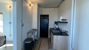 Une cuisine compacte avec un réfrigérateur noir, un évier et un plan de travail. On y trouve également un coin repas avec une table ronde et des chaises.