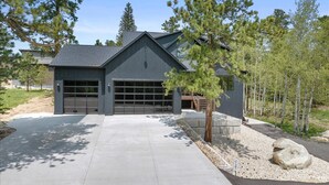 A modern two-story house with a garage, surrounded by trees and a gravel driveway.