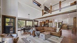 A spacious living area with a large sectional sofa, a coffee table, and a fireplace. There is a dining area with a table and chairs, and a kitchen in the background.