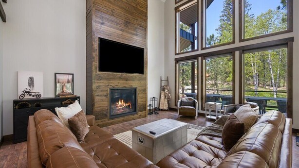 A modern living room with a fireplace, leather sofas, and large windows offering a view of the outdoors.