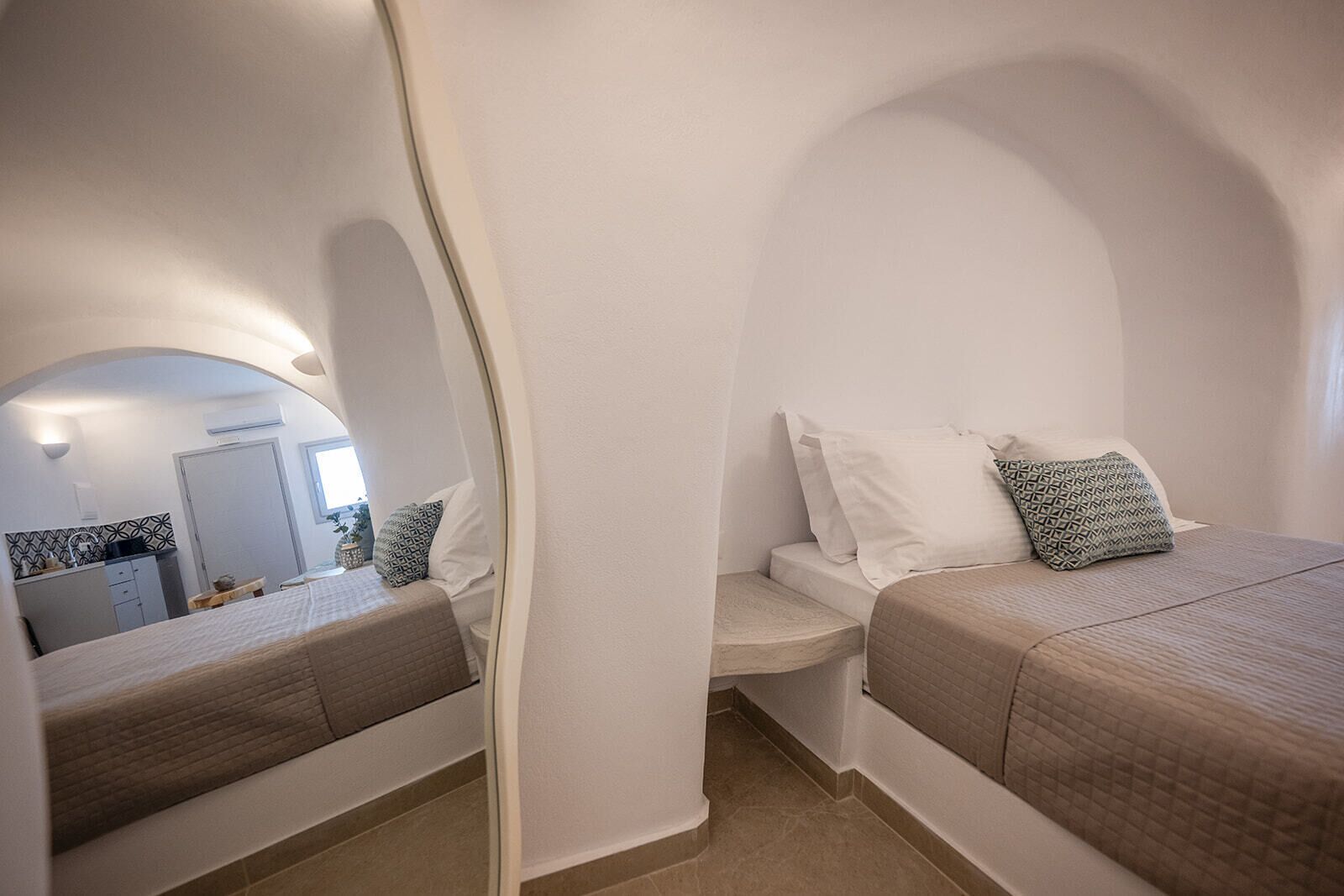 A bedroom with two beds, a small seating area, and a view of a kitchen and bathroom through an arched doorway.