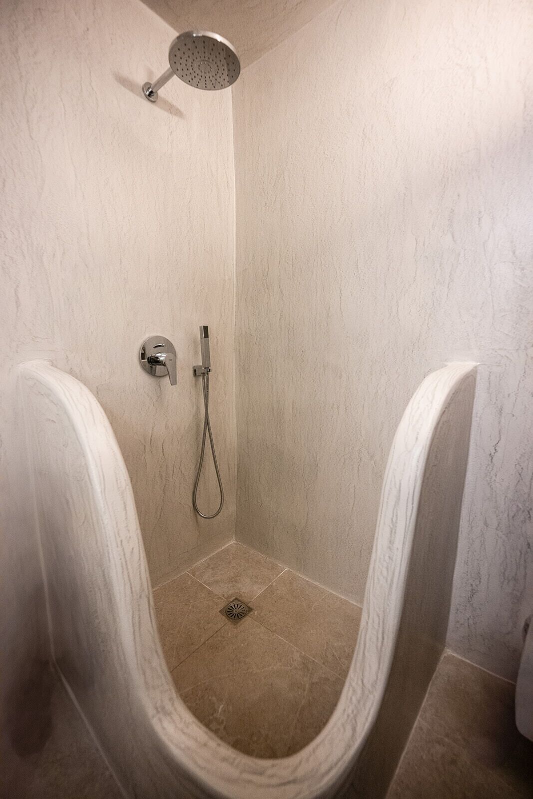 A walk-in shower with a handheld showerhead, a handheld shower attachment, and a wall-mounted faucet.