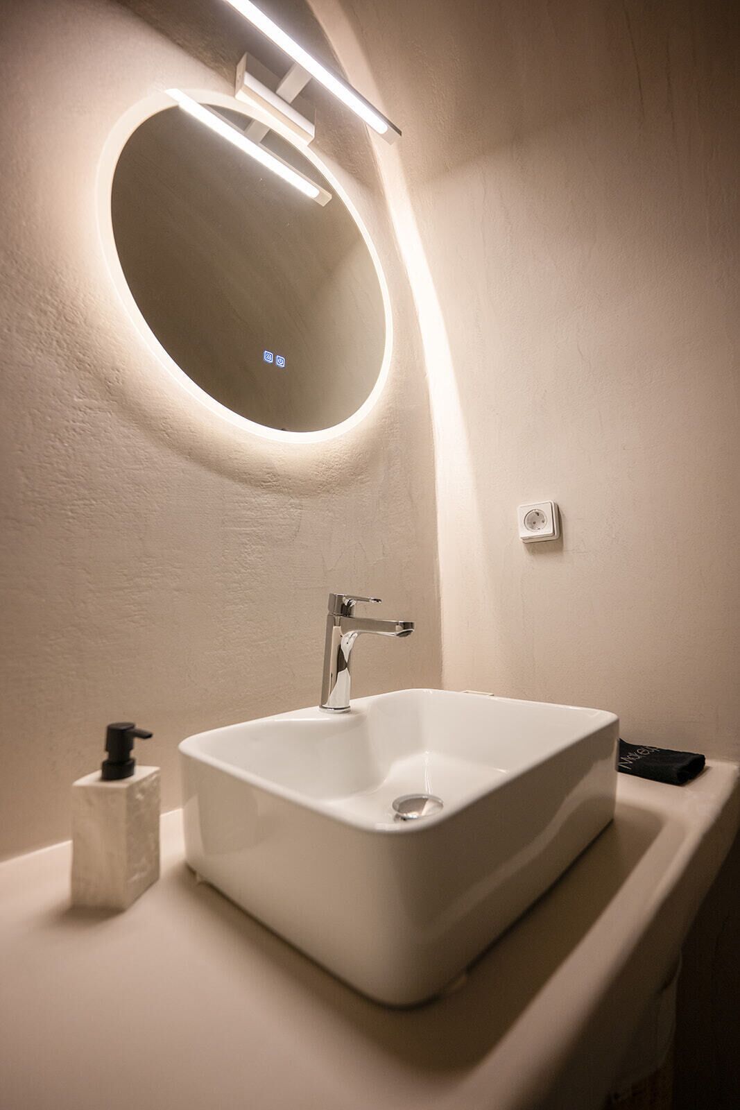 Un baño con un lavamanos blanco, un espejo con marco circular y una lámpara de pared.
