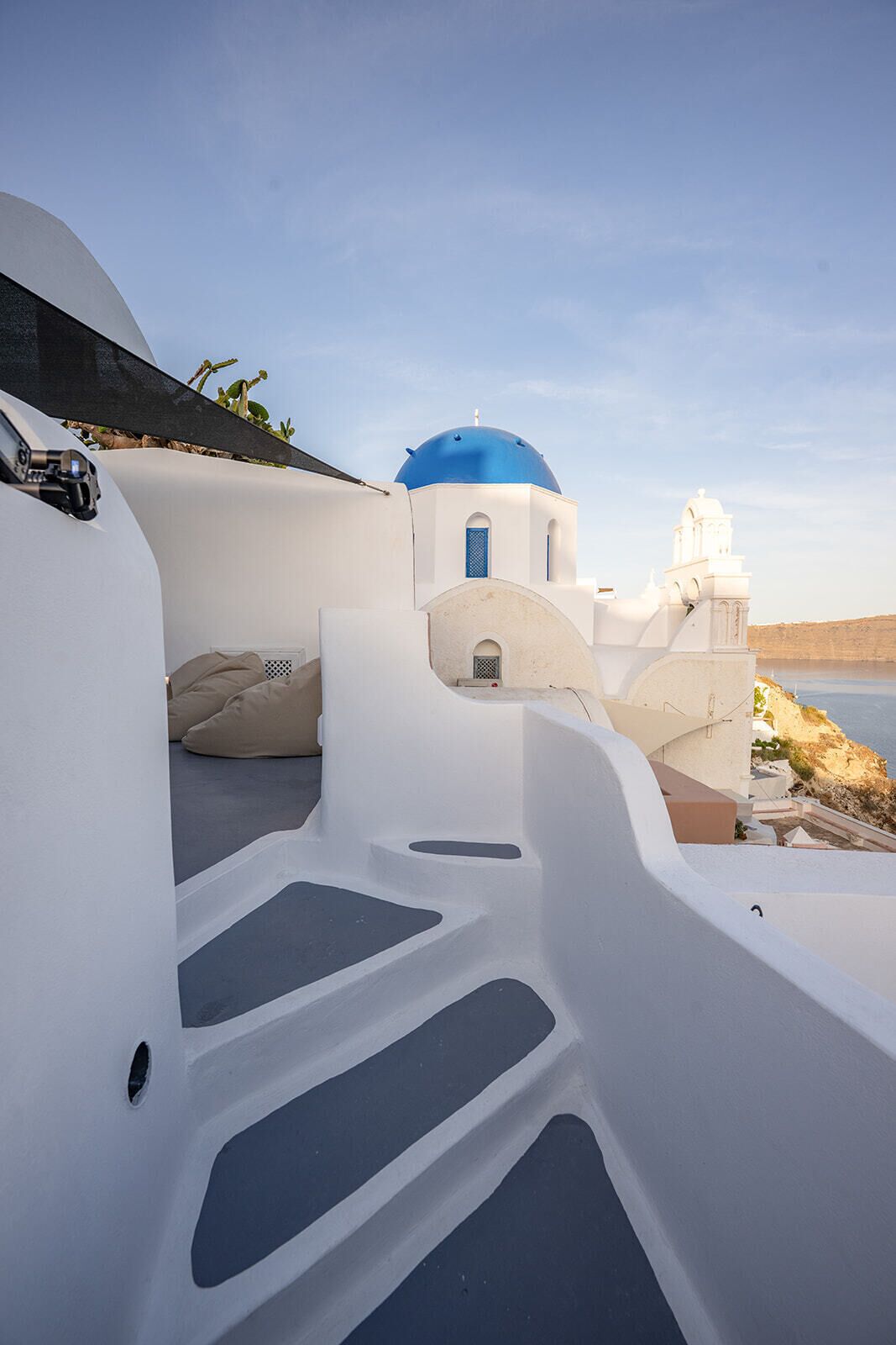 A white building with blue domes, a staircase, and a view of the sea.