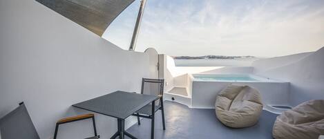 Una terraza moderna al aire libre con mesa y sillas, un área de descanso con pufs y vistas al mar.