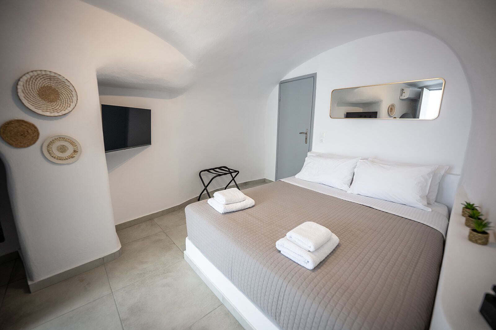 Un dormitorio moderno con una cama grande, un televisor de pantalla plana, un espejo y una pequeña planta en maceta.