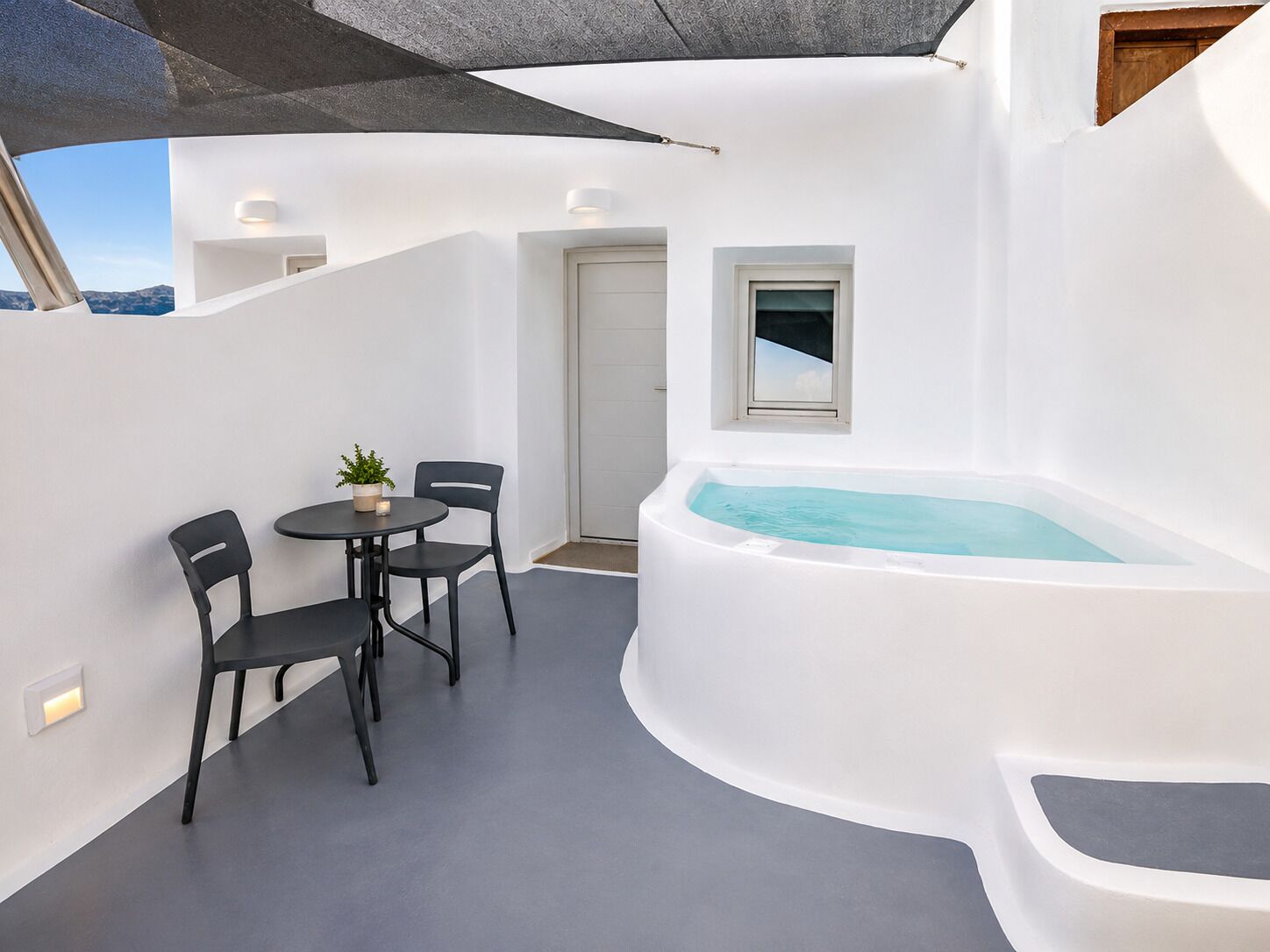 Een modern terras met een ronde tafel en stoelen, een kleine potplant en een hottub.