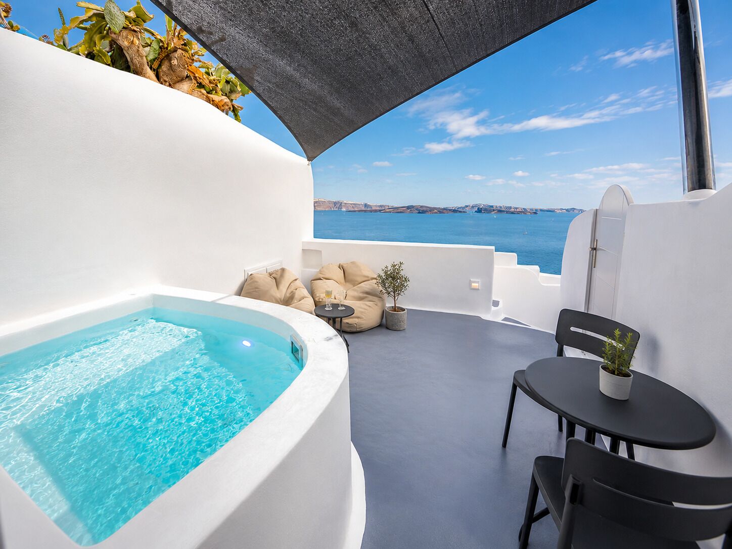 A modern outdoor balcony with a hot tub, seating area, and a view of the sea.