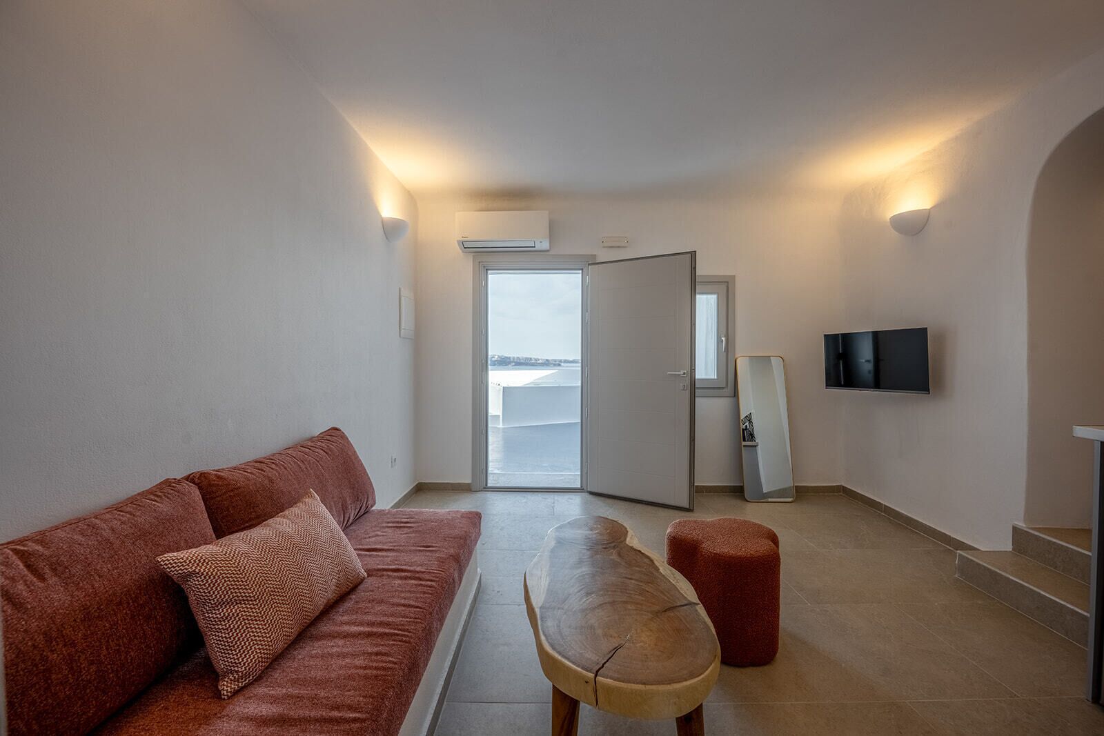 Uma sala de estar moderna com um sofá, uma mesa de madeira e uma TV fixada na parede.