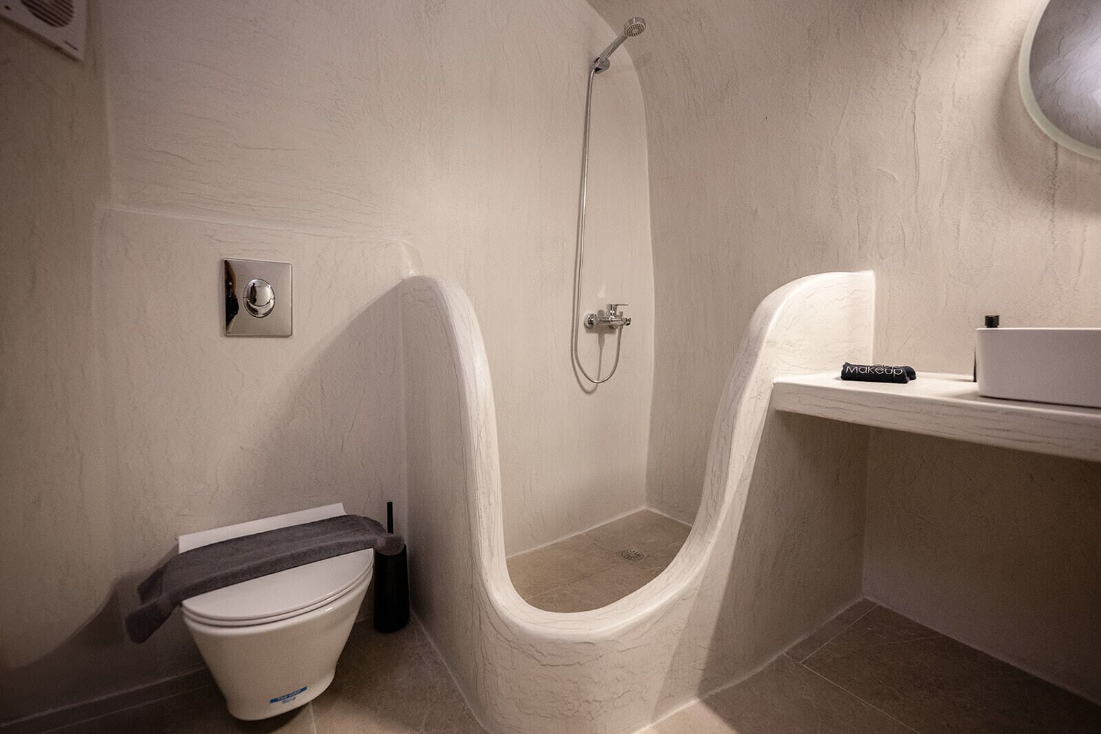 A compact bathroom with a toilet, a shower, and a small shelf with a makeup case.