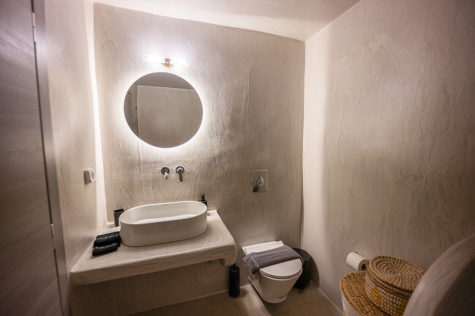 A small bathroom with a round mirror, a sink, and a toilet.